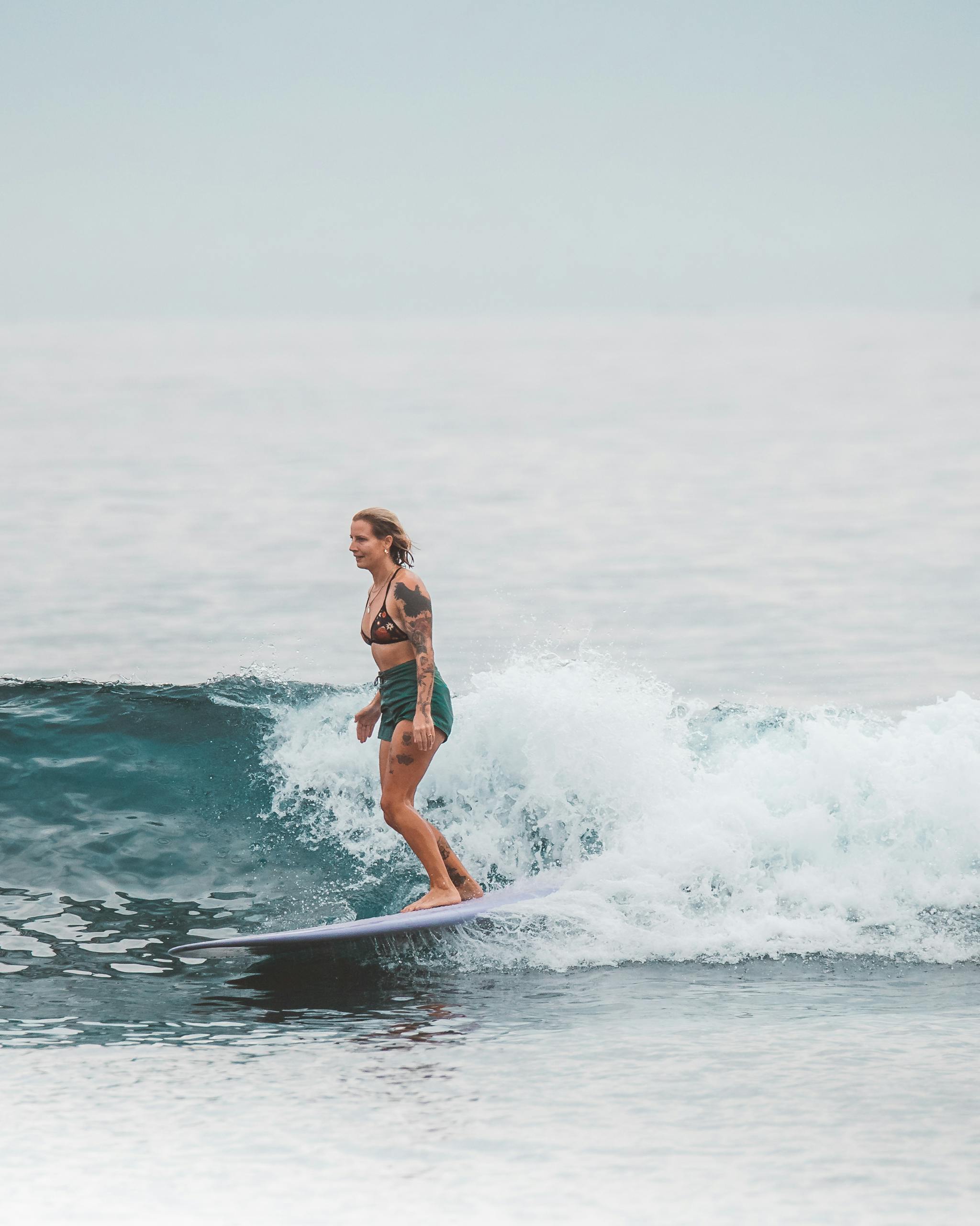 A woman surfing on a wave with a surfboard in the open ocean, showcasing her skill and balance.